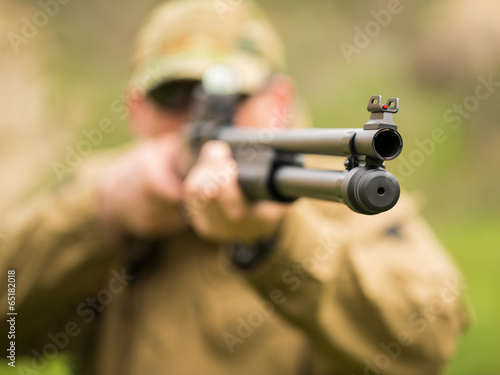 Man in camouflage with a shotgun aiming at a target