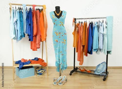 Wardrobe with orange and blue clothes on hangers and a mannequin