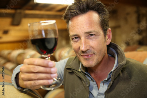 Winegrower in wine-cellar holding glass of wine