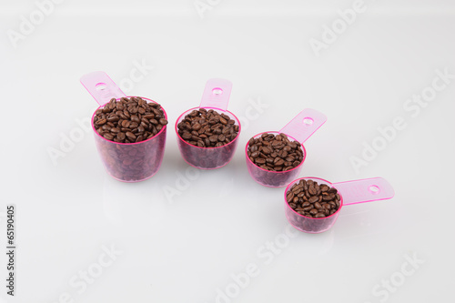 Coffee beans in measuring cups of various sizes on white photo