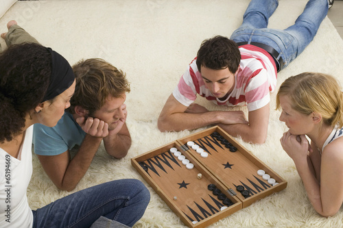 Obraz na plátne Vier junge Menschen auf dem Boden,spielen Backgammon