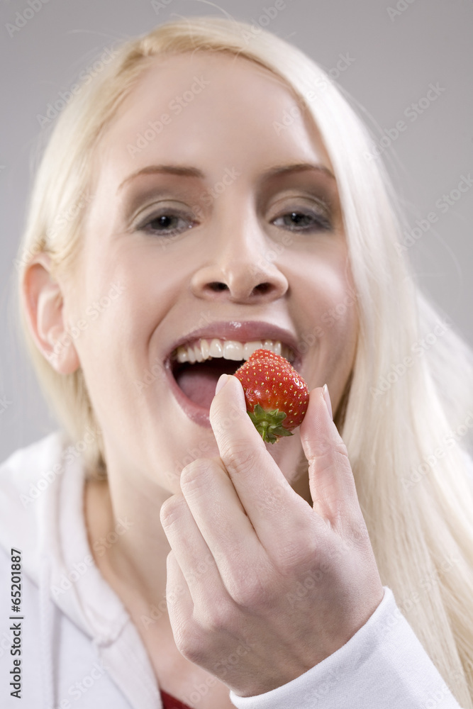 Junge Frau hält eine Erdbeere, lächelnd, Porträt Junge Frau hält eine Erdbeere, lächelnd, Porträt