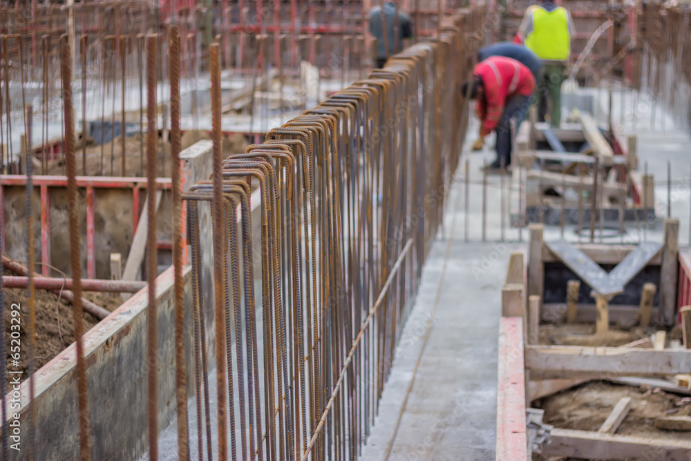 Naklejka premium Blurred workers and steel reinforcement in foundation of new bu