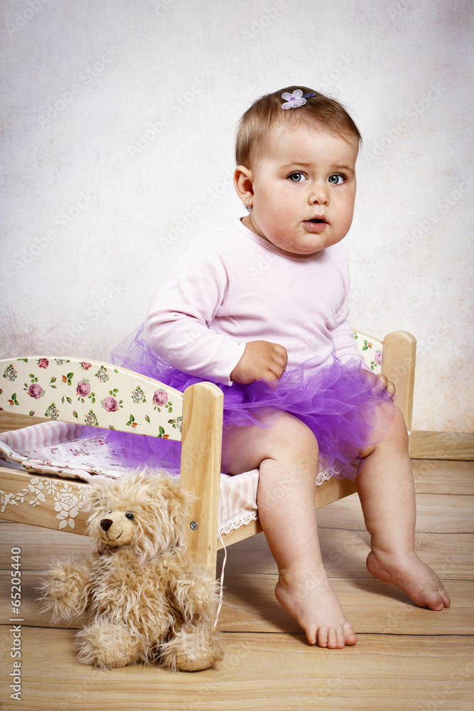 Beautiful little baby girl sitting on the bed with teddy bear