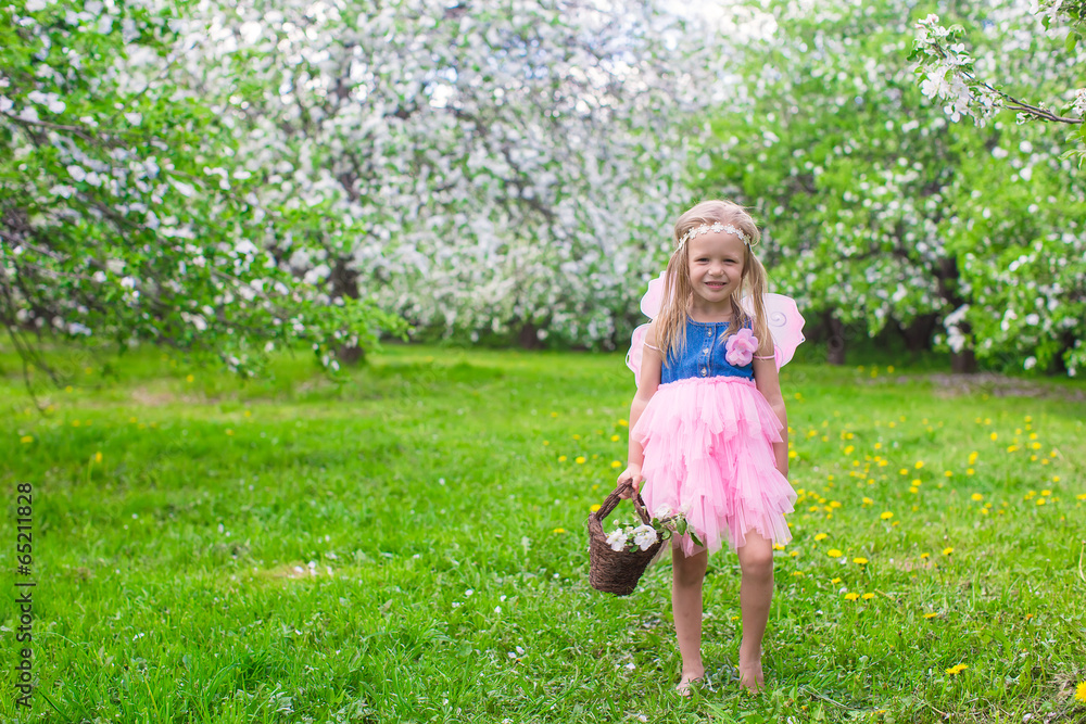 Adorable little girl with straw basket in blossoming apple