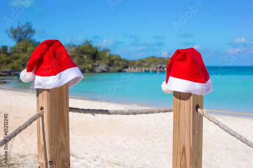 Close-up two Santa hats on fence at tropical white beach