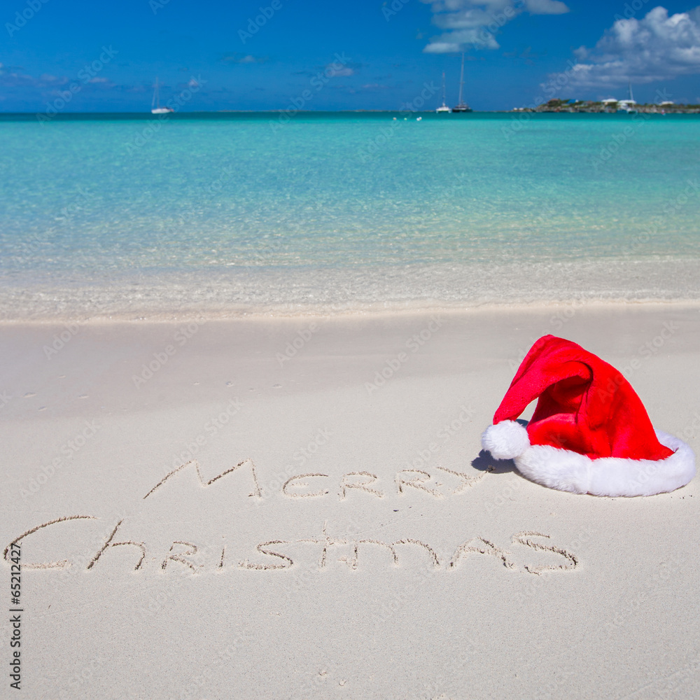 Santa Hat on white sandy beach and Merry Christmas written in Santa Hat on white sandy beach and Merry Christmas written in