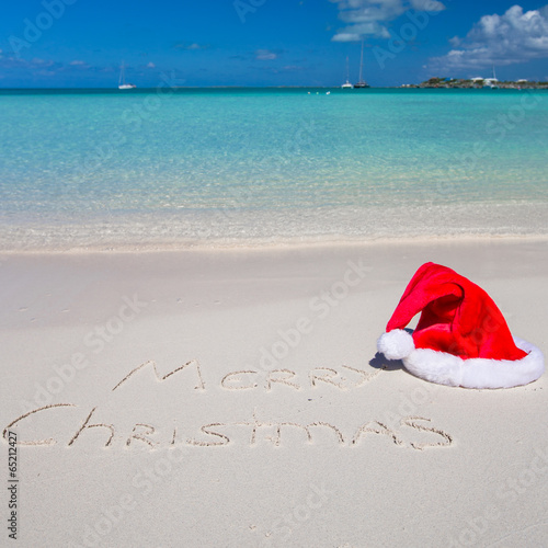 Santa Hat on white sandy beach and Merry Christmas written in