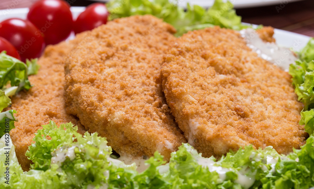 Fried battered chicken breast fillet with lettuce on the plate Fried battered chicken breast fillet with lettuce on the plate