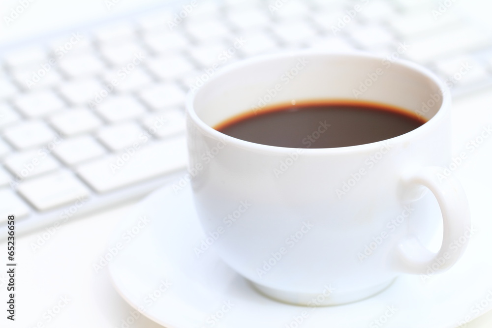 White cup of coffee in front of computer keyboard