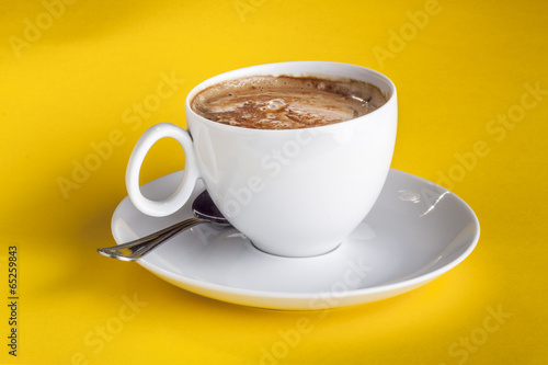 Coffee cup and saucer on a yellow background.