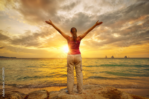 Young woman with raised hands standing on shore and looking to a