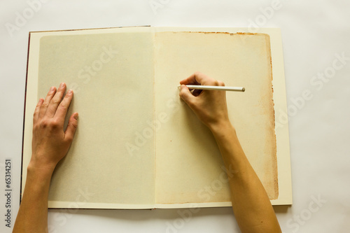Human hands writing on blank pages of opened vintage book 