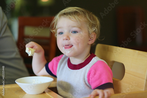 Adorable toddler girl eating ice cream in cafe