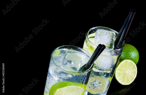 two glasses with cocktail and ice with lime slice on black table