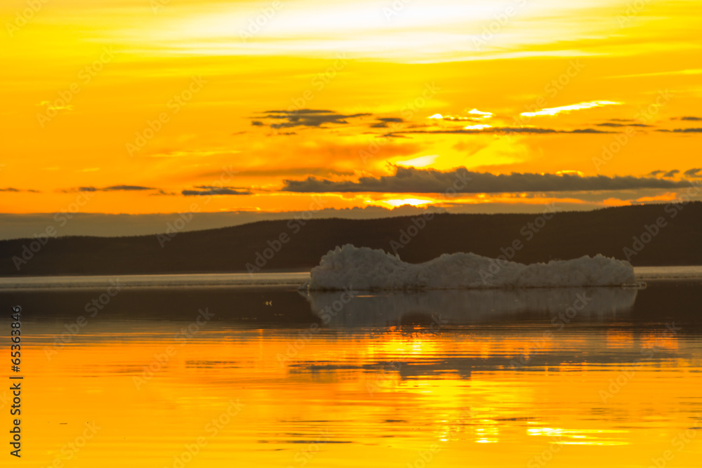 The melting iceberg on spring mountain lake in the setting sun.