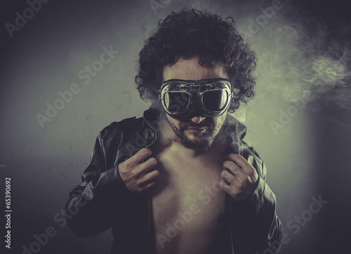 Biker, man with googles and black coat, smoke and dark backgroun