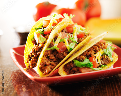 three beef tacos with cheese, lettuce and tomatos