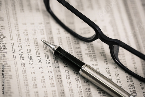 closeup glasses on financial newspaper with pen