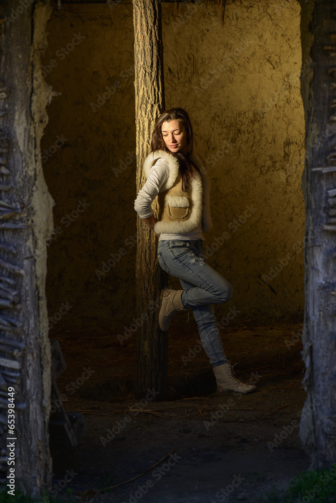Young woman leaning against a timber pole on a dark room