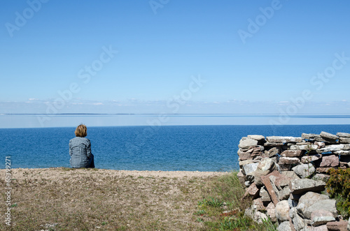 Woman sitting by the coast looking at clear blue sky and water © olandsfokus