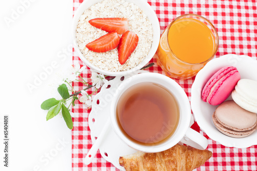Tea cup with croissant, colourful french macaroons, oatmeal with