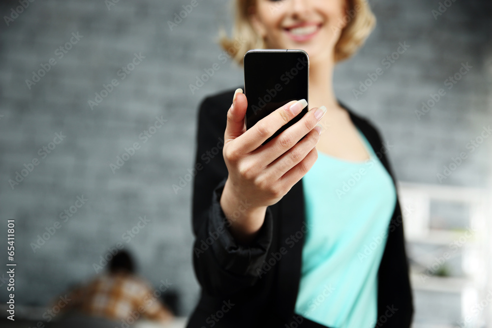 Happy woman holding smartphone in office. Focus on smartphone