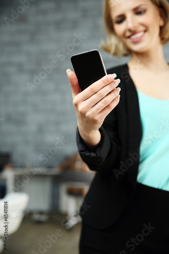 Happy woman holding smartphone in office. Focus on smartphone