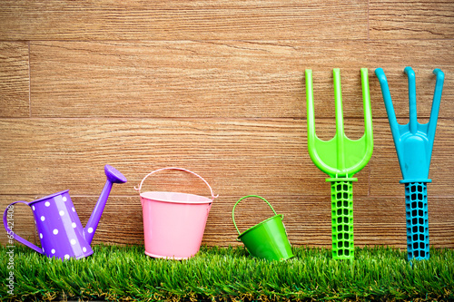 watering cans, pails, fork, rake on grass with wood background