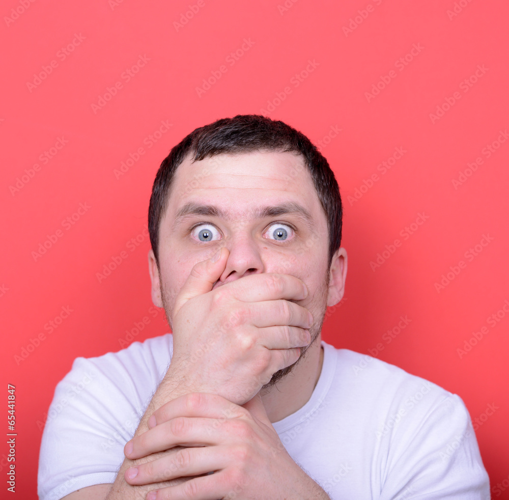 Portrait of man with hands covering mouth against red background