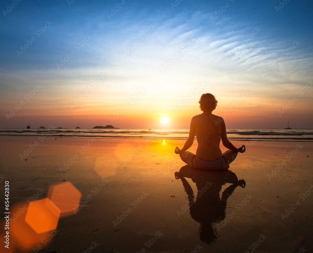 Woman meditating on the beach at sunset.