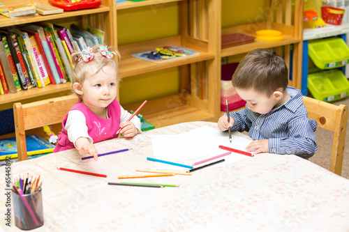 Two little kids drawing with colorful pencils in preschool