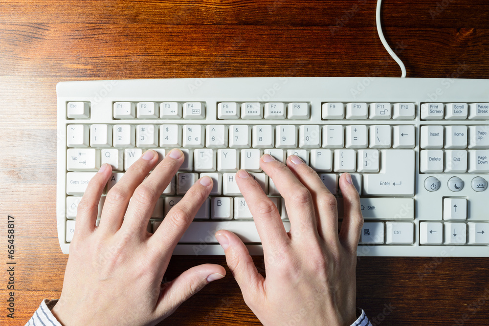 Woman hands typing on a white keyboard on wooden background Woman hands typing on a white keyboard on wooden background