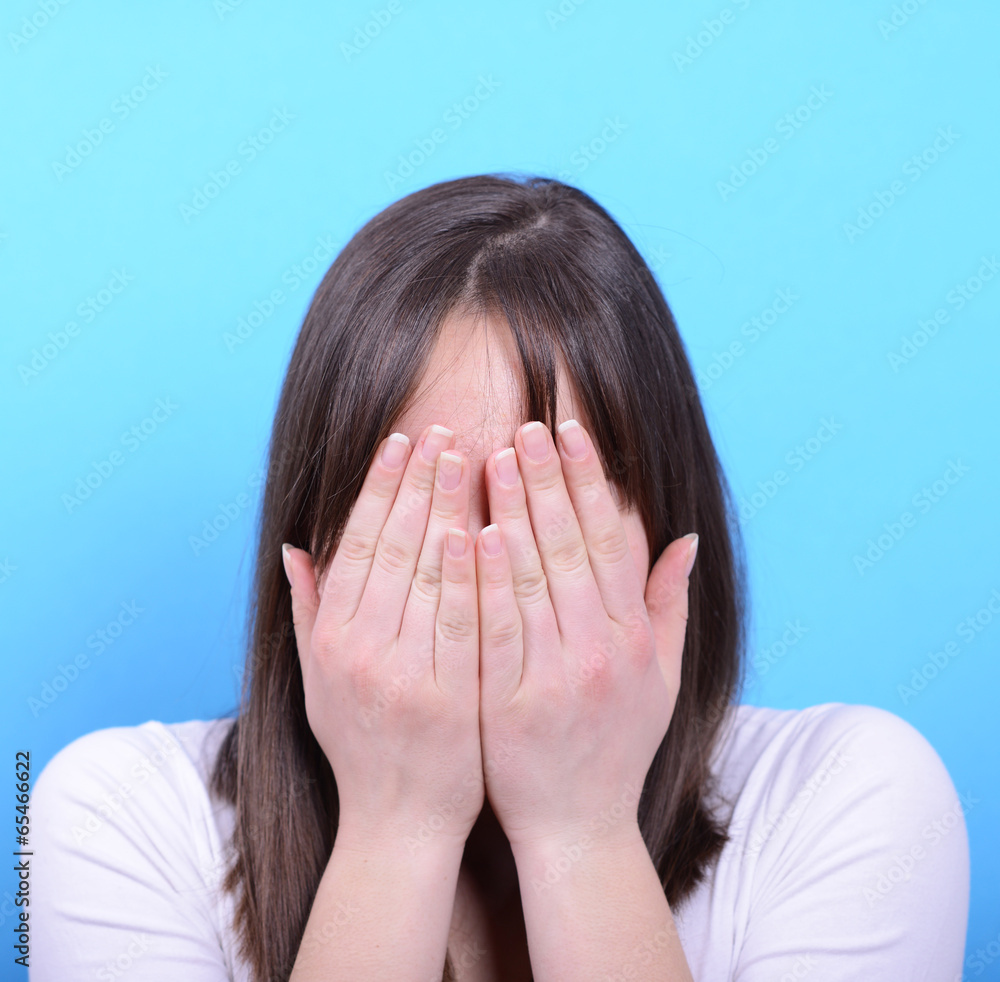 Portrait of covering her face with hands against blue background Portrait of covering her face with hands against blue background