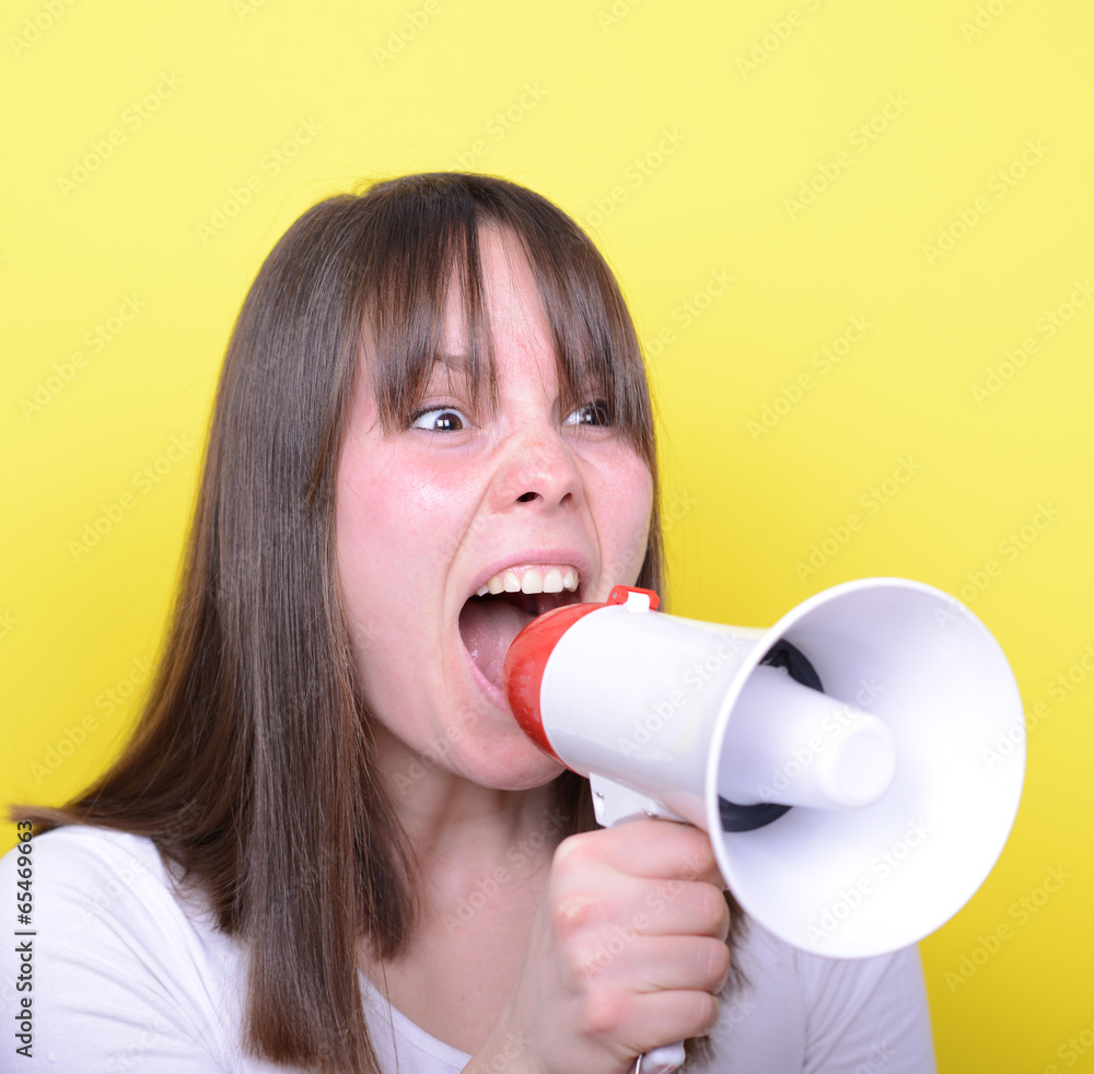 Portrait of young woman shouting with a megaphone against yellow Portrait of young woman shouting with a megaphone against yellow