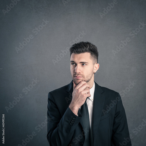 Young businessman portrait thinking against dark grunge backgrou