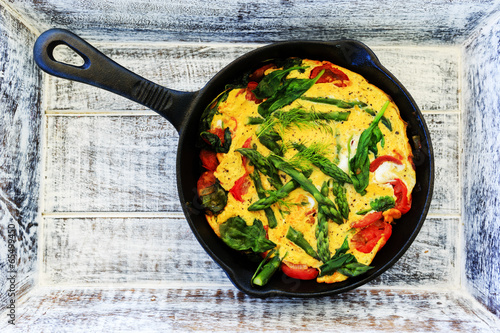 Omelette with asparagus and tomato on frying pan