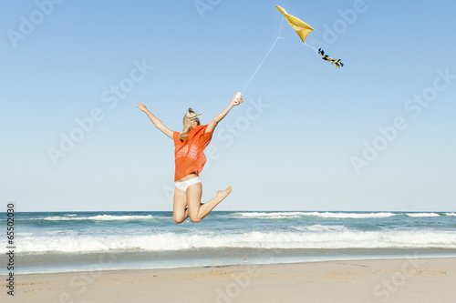 young attractive girl jumping with yellow kite on beach