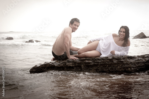 Young beautiful couple sharing moment on beach rocks