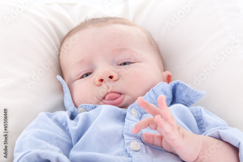 Baby boy lying on the bed and sticking his tongue out