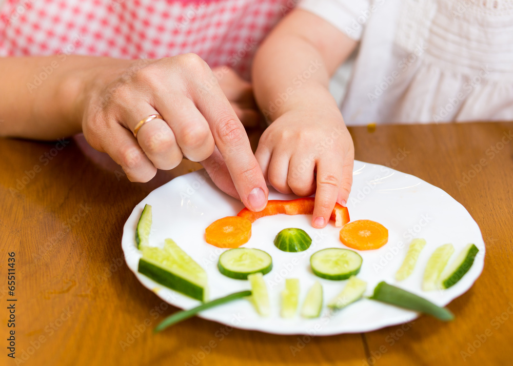 mother and kid girl making funny face from vegetables on plate