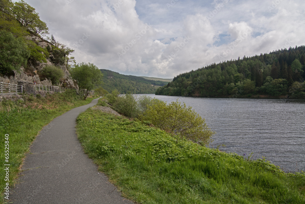 Fototapeta premium Footpath alongside a picturesque lake, with wooded hills