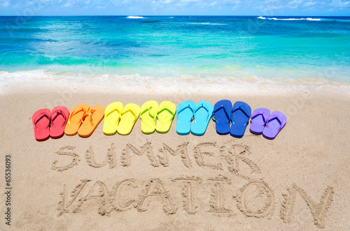 Sign "Summer vacation" and color flip flops on sandy beach