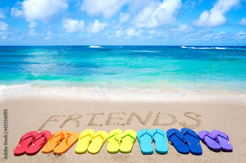Sign "Friends" and color flip flops on sandy beach
