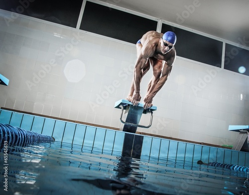 Young muscular swimmer in low position on starting block