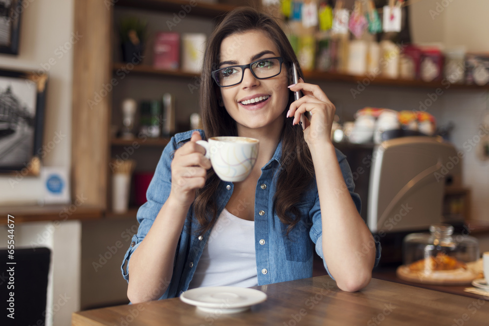 Smiling young woman talking by mobile phone at cafe Smiling young woman talking by mobile phone at cafe