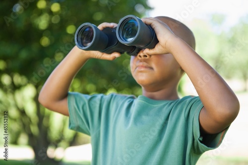 Little boy looking up through binoculars in the park