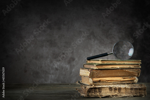 Pile of old antique and yellowed books with a magnifying glass