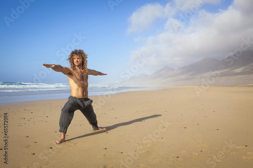 young man doing yoga warrior pose on the beach