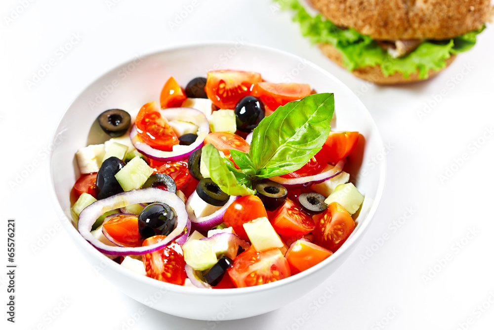 Light greek salad with fresh vegetables and burger in the backgr